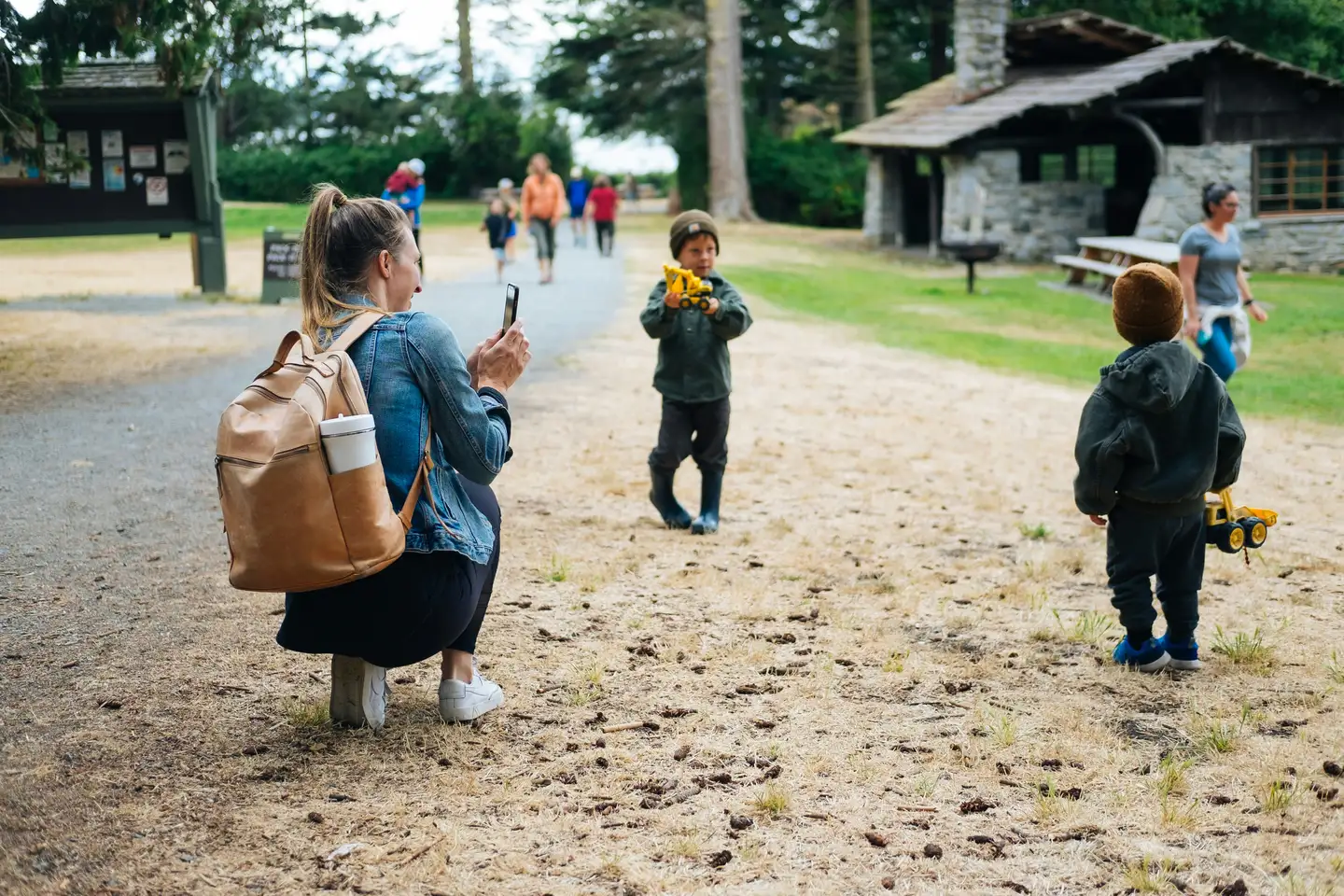 Pedagog på huk som fotograferar ett barn med en leksaksbil utomhus.