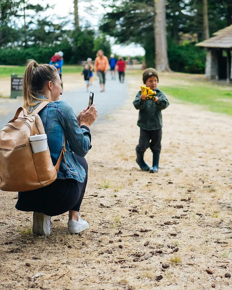 Pedagog på huk som fotograferar ett barn med en leksaksbil utomhus.